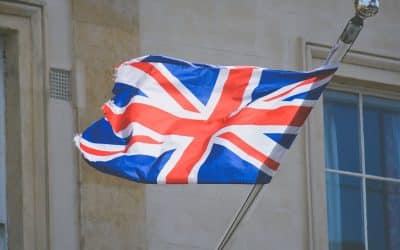 Union Jack flag fluttering from a pole against a pale stone building facade