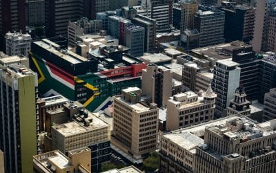 Aerial view of a dense city skyline with a large South African flag painted on a downtown rooftop