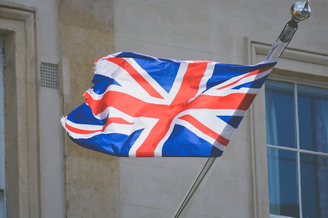 Union Jack flag fluttering from a pole against a pale stone building facade