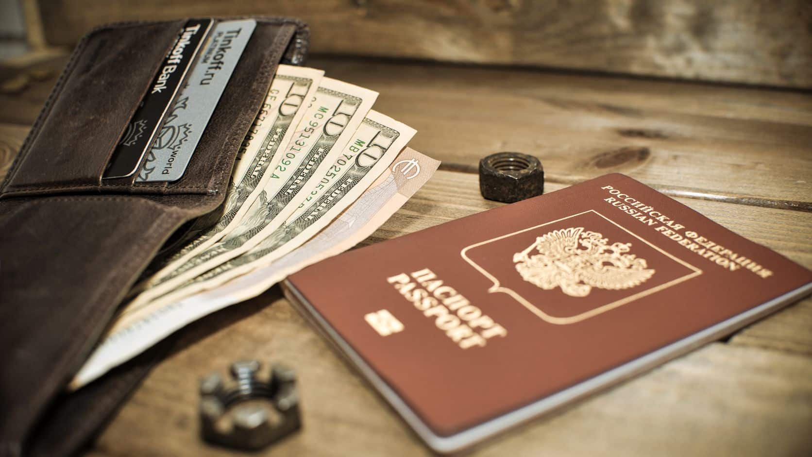 Passport, wallet, and dollar bills arranged on a wooden table