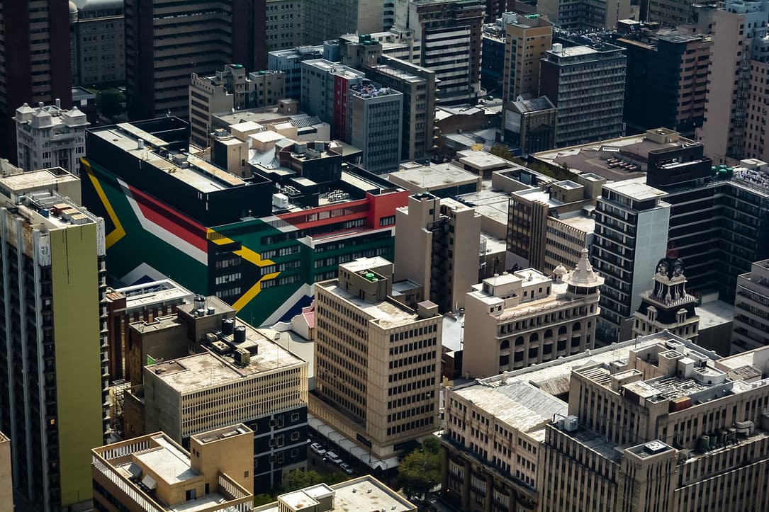 Aerial view of a dense city skyline with a large South African flag painted on a downtown rooftop