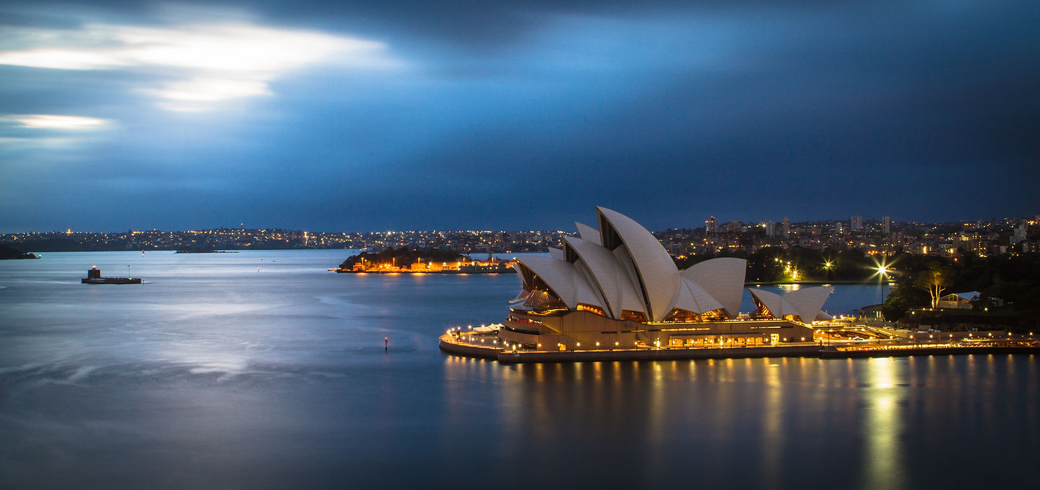 Sydney Opera House lit up on the harbour at dusk with the city skyline behind