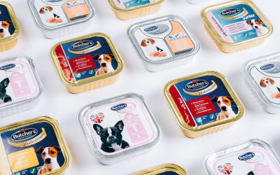 Many sealed trays of Butcher's brand wet dog food in different varieties arranged on a white surface