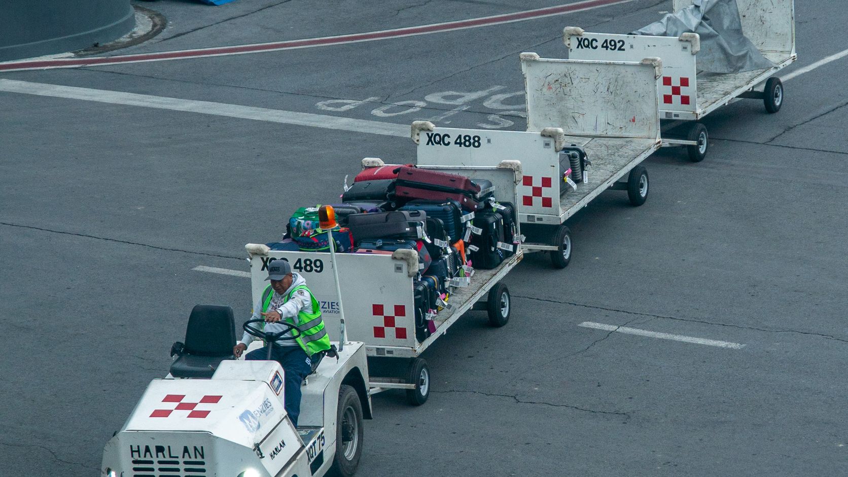 Airport ground crew member towing baggage carts across the tarmac