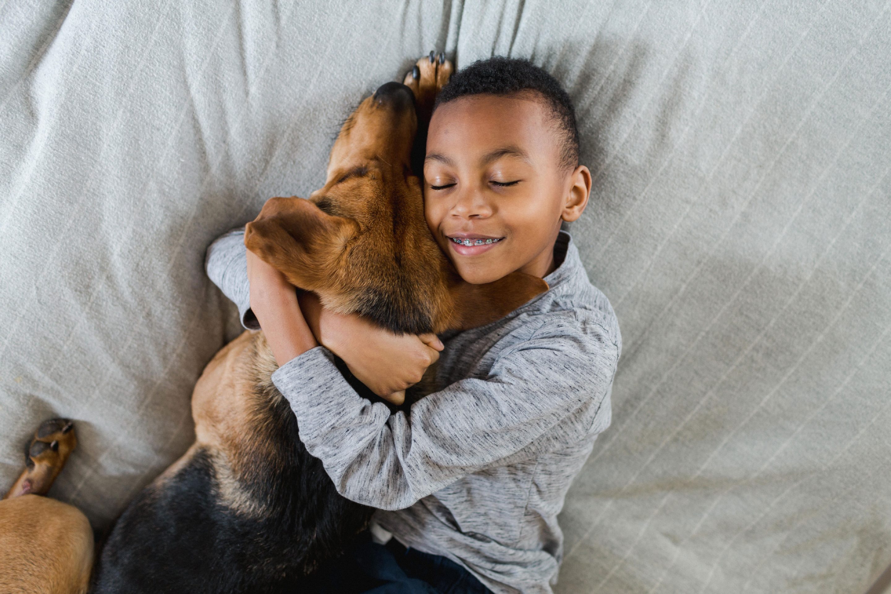 Boy hugging black tan dog on bed