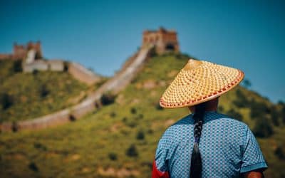 A person in a woven straw hat looking out over the Great Wall of China on a green hillside